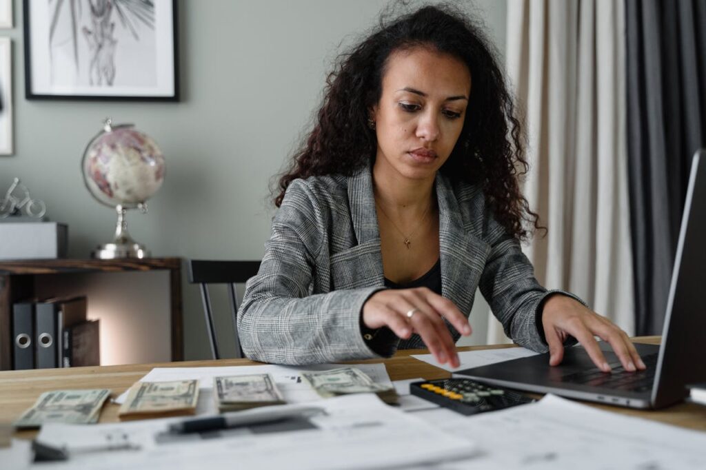 Female business owner in a plaid blazer using her laptop and mobile phone.